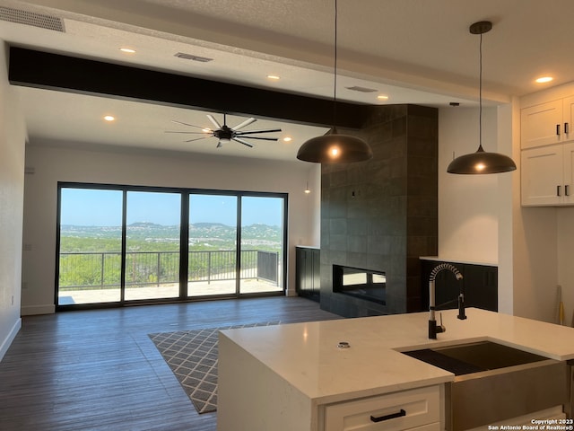 kitchen featuring pendant lighting, light stone countertops, beamed ceiling, white cabinetry, and a tiled fireplace