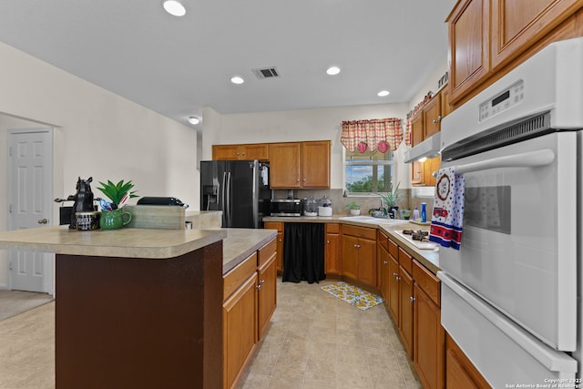 kitchen featuring white appliances, sink, light tile floors, a center island, and tasteful backsplash