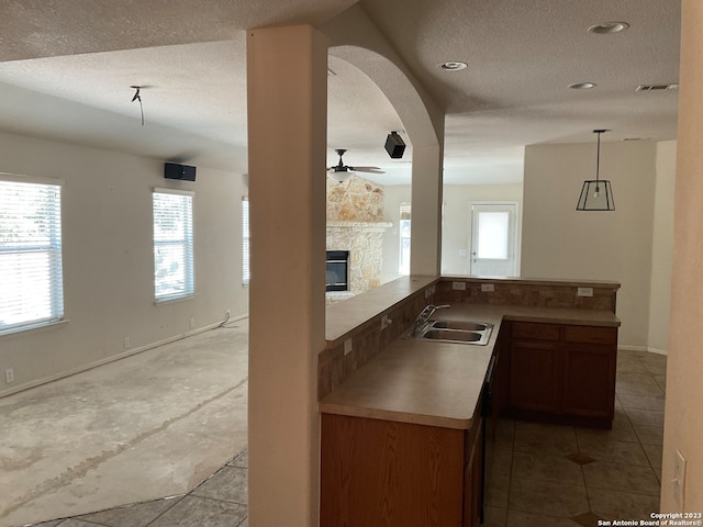 kitchen with plenty of natural light, sink, a stone fireplace, and pendant lighting