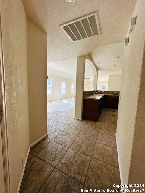 hallway featuring lofted ceiling, a textured ceiling, and tile floors