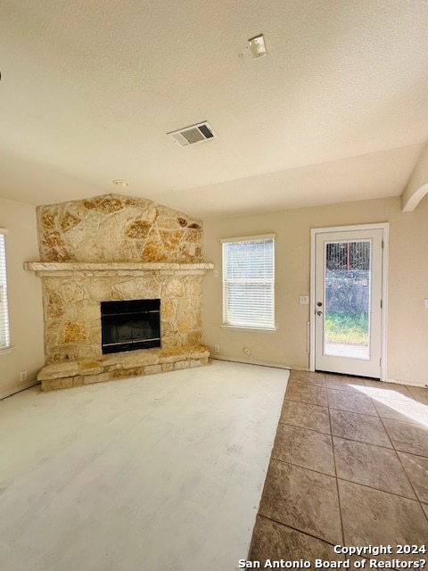 unfurnished living room with a textured ceiling, light tile flooring, and a stone fireplace