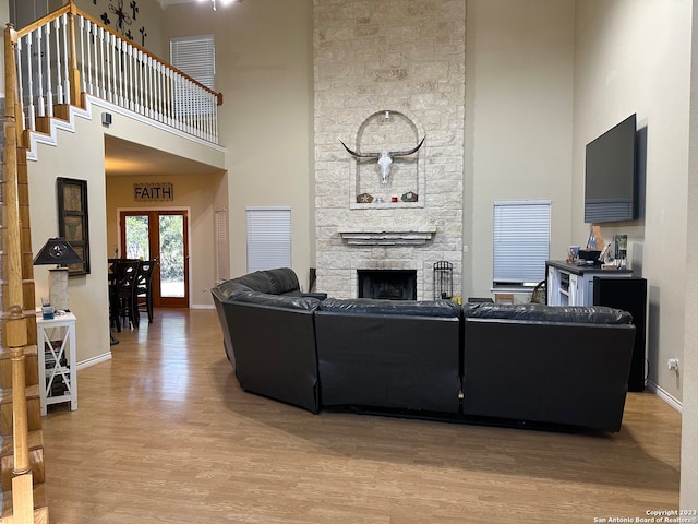 living room with french doors, light hardwood / wood-style floors, a stone fireplace, and a towering ceiling