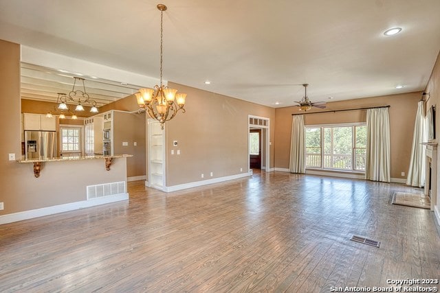 unfurnished living room with wood-type flooring, beam ceiling, and ceiling fan with notable chandelier