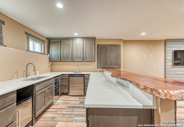 kitchen with sink, light stone countertops, light hardwood / wood-style floors, and stainless steel dishwasher