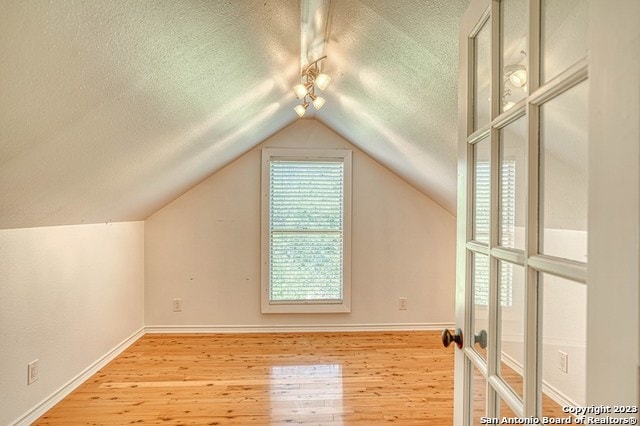 additional living space featuring light hardwood / wood-style flooring, lofted ceiling, and a textured ceiling