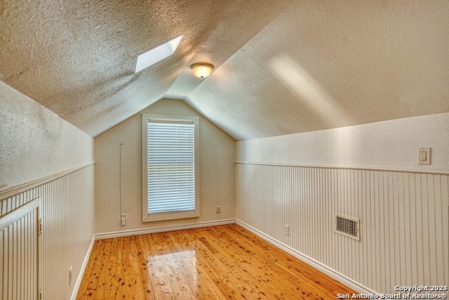 bonus room featuring light hardwood / wood-style floors, lofted ceiling with skylight, and a textured ceiling