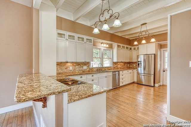 kitchen with appliances with stainless steel finishes, decorative light fixtures, beam ceiling, a chandelier, and kitchen peninsula