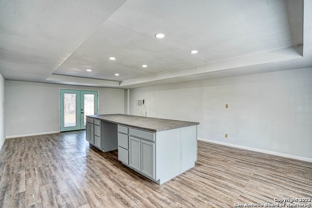 kitchen featuring french doors, a kitchen island, light hardwood / wood-style flooring, a tray ceiling, and gray cabinetry