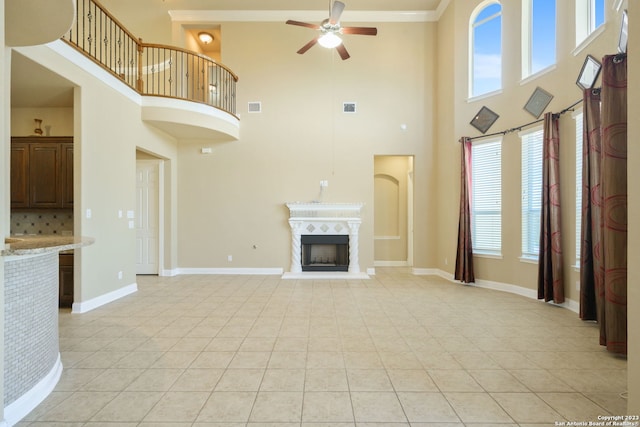 unfurnished living room featuring a tiled fireplace, ornamental molding, ceiling fan, and a towering ceiling