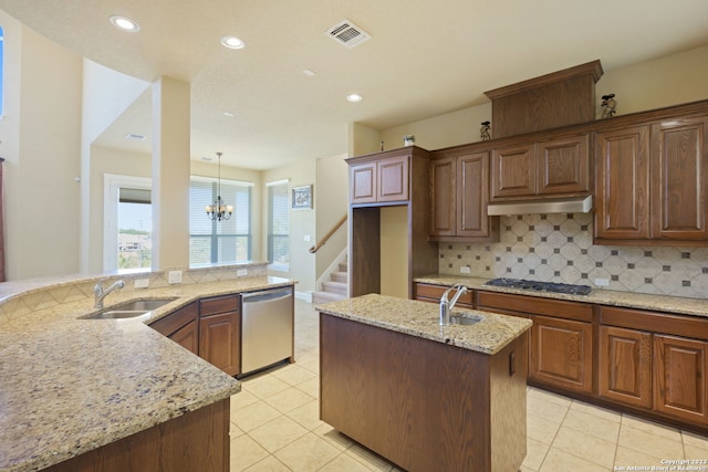 kitchen with light stone counters, a chandelier, backsplash, stainless steel appliances, and wall chimney exhaust hood