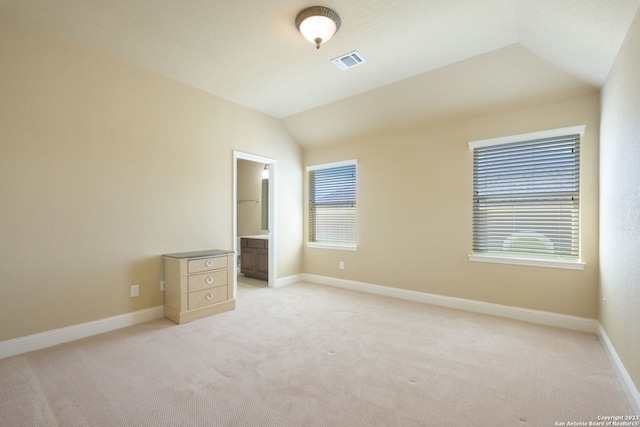 unfurnished bedroom with light carpet, a spacious closet, ensuite bathroom, and vaulted ceiling