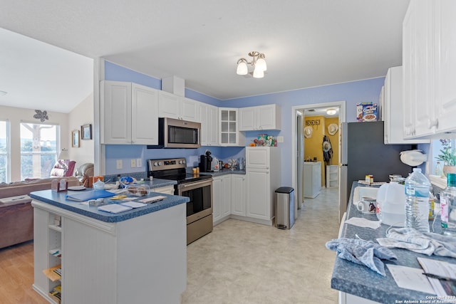 kitchen featuring kitchen peninsula, appliances with stainless steel finishes, washer / dryer, lofted ceiling, and white cabinetry