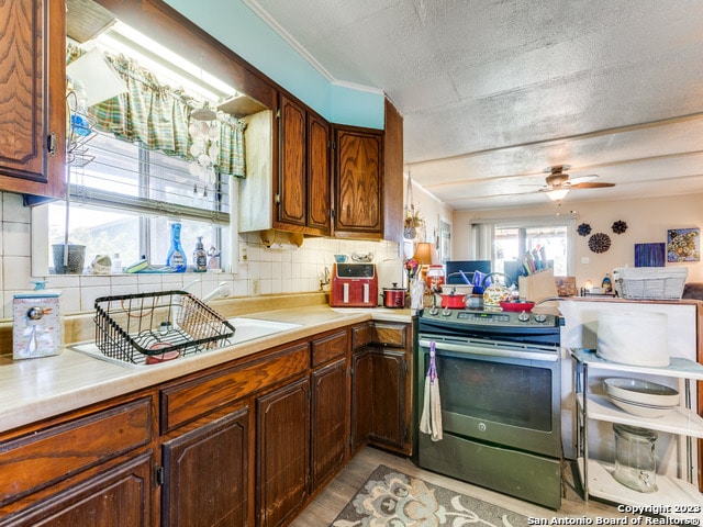 kitchen with ceiling fan, a textured ceiling, stainless steel electric stove, light hardwood / wood-style flooring, and backsplash