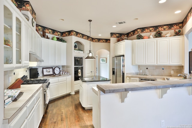 kitchen with hanging light fixtures, dark hardwood / wood-style floors, black appliances, tasteful backsplash, and a breakfast bar area