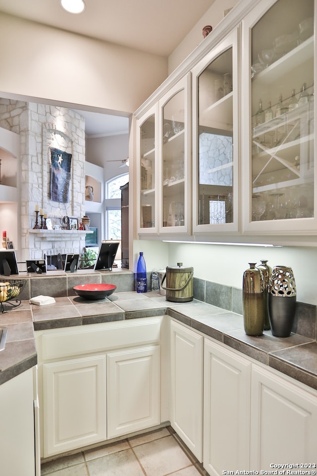 kitchen featuring light tile floors, white cabinets, and a stone fireplace