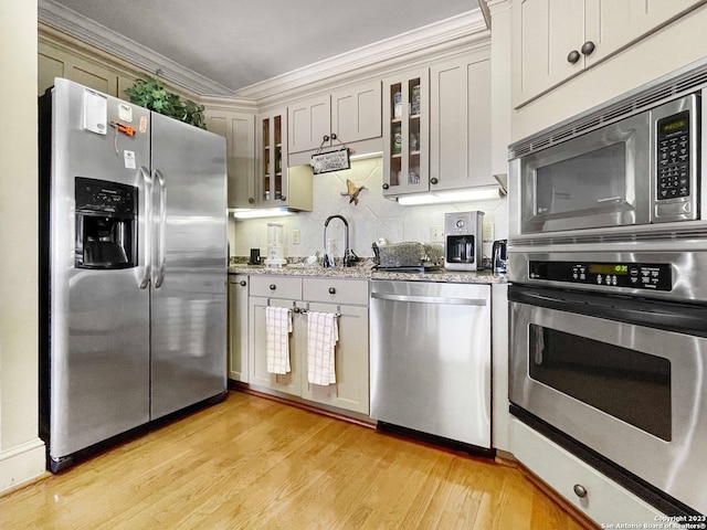 kitchen featuring backsplash, light wood-type flooring, stainless steel appliances, white cabinets, and light stone counters