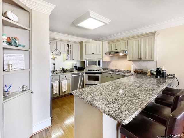 kitchen with kitchen peninsula, exhaust hood, appliances with stainless steel finishes, light hardwood / wood-style floors, and a kitchen bar