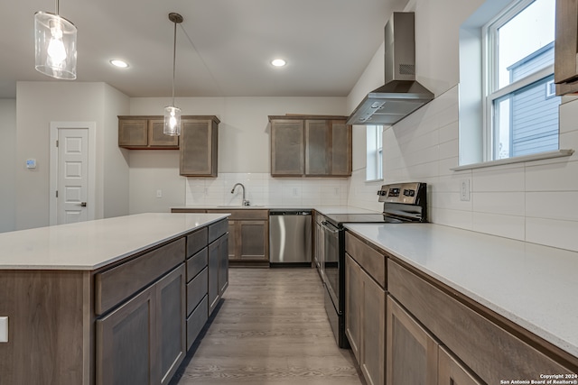 kitchen featuring decorative backsplash, appliances with stainless steel finishes, wall chimney exhaust hood, hardwood / wood-style floors, and hanging light fixtures