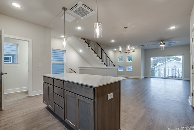 kitchen featuring pendant lighting, ceiling fan with notable chandelier, light wood-type flooring, a kitchen island, and dark brown cabinetry