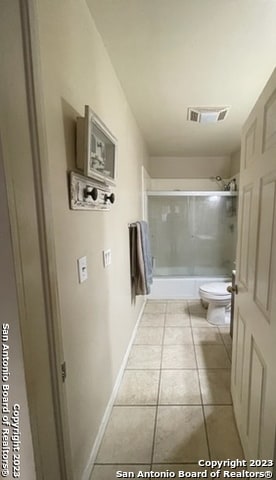 bathroom featuring toilet, tile patterned floors, and bath / shower combo with glass door