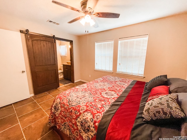 bedroom featuring a barn door, ceiling fan, dark tile flooring, and ensuite bathroom