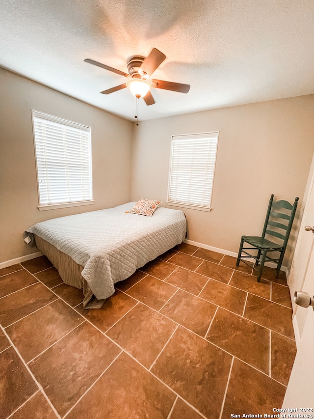 bedroom with dark tile flooring, a textured ceiling, ceiling fan, and multiple windows