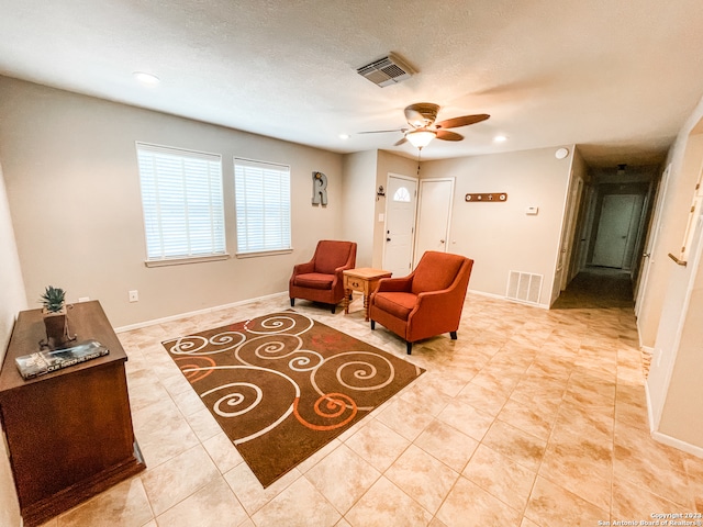 living area with light tile floors, ceiling fan, and a textured ceiling