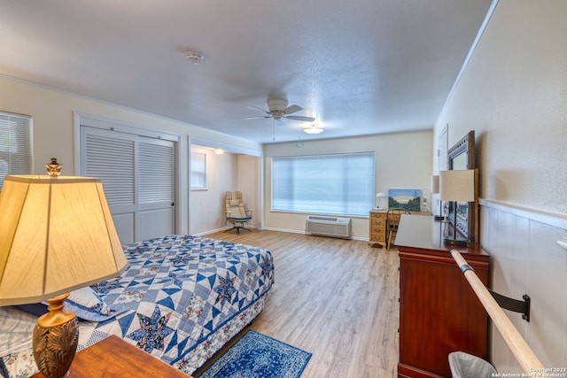 bedroom featuring light hardwood / wood-style floors, a closet, ceiling fan, and an AC wall unit