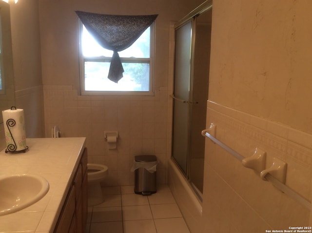 full bathroom featuring vanity, tile walls, tile flooring, toilet, and shower / bath combination with glass door