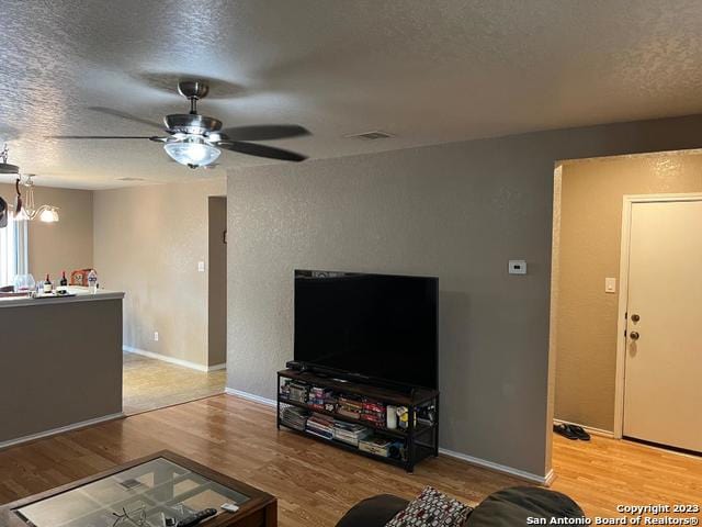 living room featuring light hardwood / wood-style floors, a textured ceiling, and ceiling fan with notable chandelier