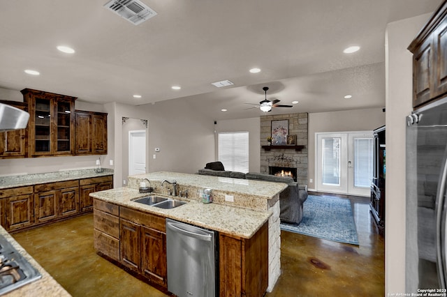 kitchen featuring ceiling fan, a kitchen island with sink, sink, dishwasher, and a stone fireplace