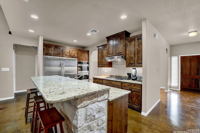 kitchen with a kitchen island, a breakfast bar area, stainless steel appliances, a textured ceiling, and light stone countertops