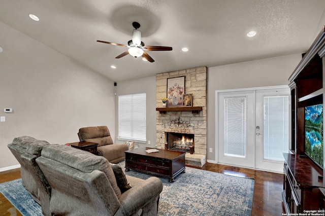 living room with dark hardwood / wood-style floors, ceiling fan, a textured ceiling, a stone fireplace, and french doors