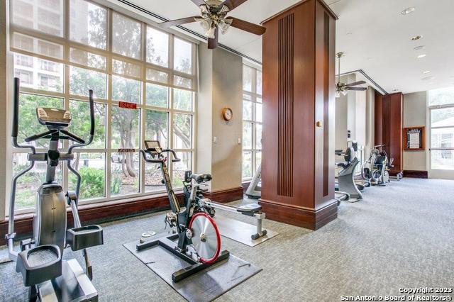 gym with a high ceiling, floor to ceiling windows, carpet, and ceiling fan