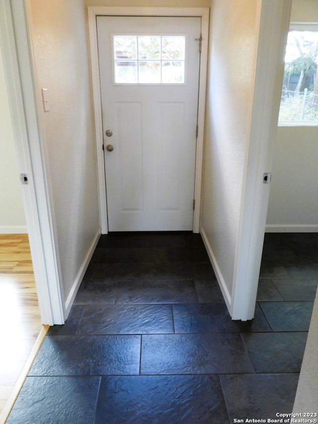 doorway with baseboards, a healthy amount of sunlight, and stone tile floors