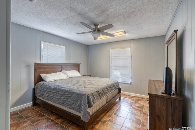 bedroom featuring wood walls, ceiling fan, a textured ceiling, and dark tile flooring