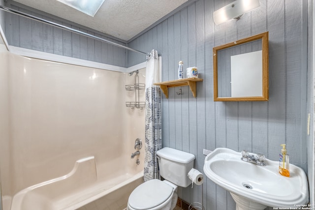 full bathroom with toilet, a textured ceiling, wooden walls, shower / bath combination with curtain, and sink