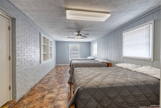 tiled bedroom with a textured ceiling, brick wall, and ceiling fan