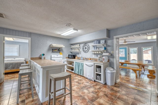 kitchen featuring a kitchen bar, ceiling fan, a textured ceiling, white appliances, and dark tile floors