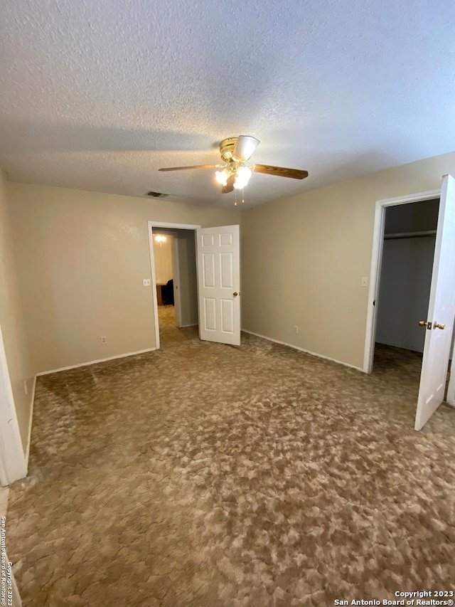 unfurnished bedroom with a walk in closet, a textured ceiling, ceiling fan, and dark carpet