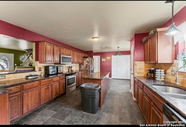 kitchen with dark tile floors, hanging light fixtures, tasteful backsplash, and stainless steel appliances