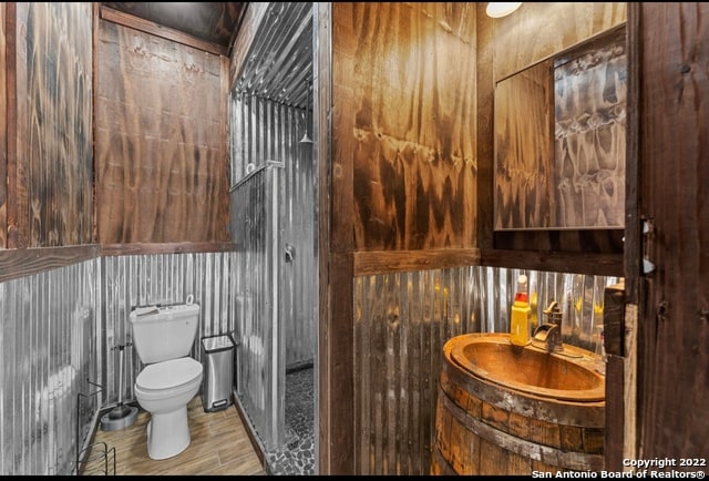 bathroom featuring toilet, wood walls, and hardwood / wood-style flooring