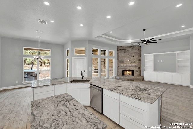 kitchen featuring ceiling fan with notable chandelier, a fireplace, a sink, visible vents, and dishwasher