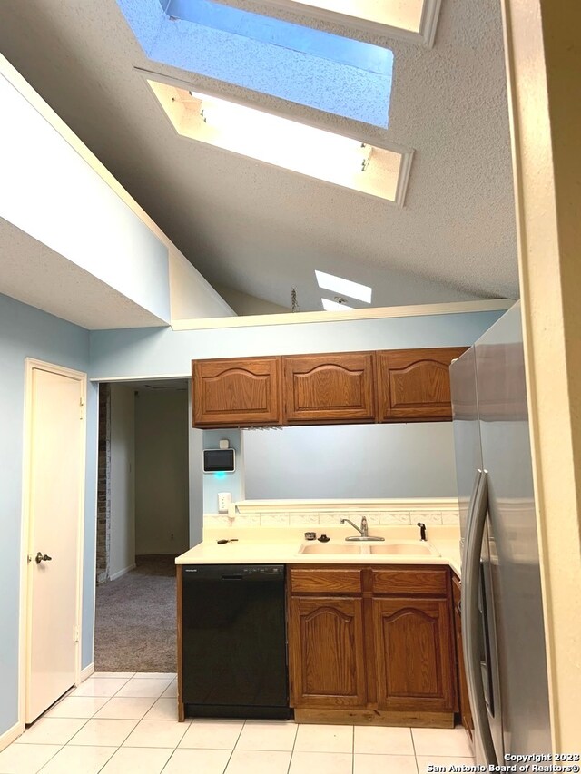 kitchen featuring lofted ceiling with skylight, sink, black dishwasher, stainless steel refrigerator, and a textured ceiling