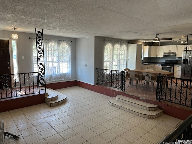 living room featuring a textured ceiling, light tile flooring, ceiling fan, and sink