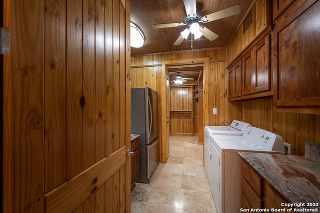 clothes washing area featuring ceiling fan, cabinets, wooden walls, and washer and clothes dryer