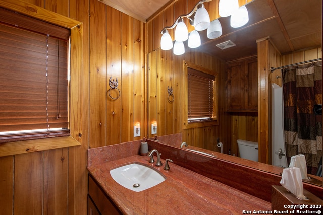 bathroom featuring a shower with shower curtain, wood walls, vanity, and toilet