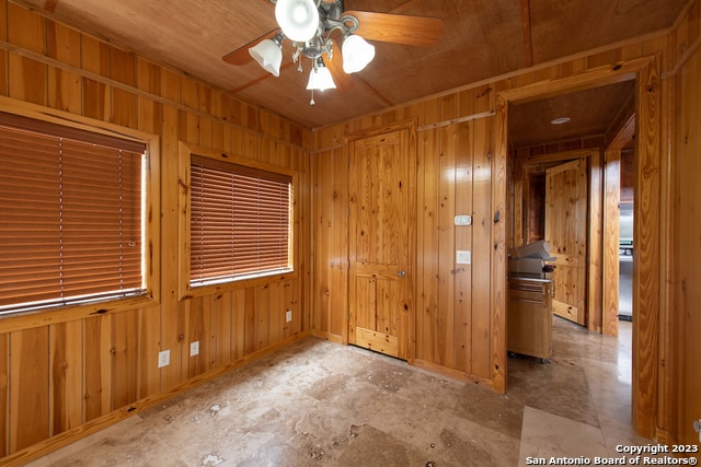 empty room with ceiling fan, wood walls, and wooden ceiling