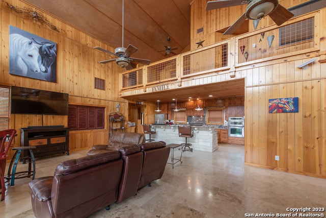 living room with wooden walls, ceiling fan, and high vaulted ceiling