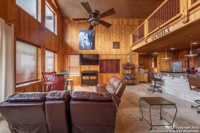 living room featuring wood walls, a towering ceiling, and ceiling fan